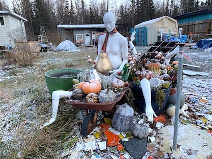 wheelbarrow filled with gourds sitting near a mannequin wearing a tie