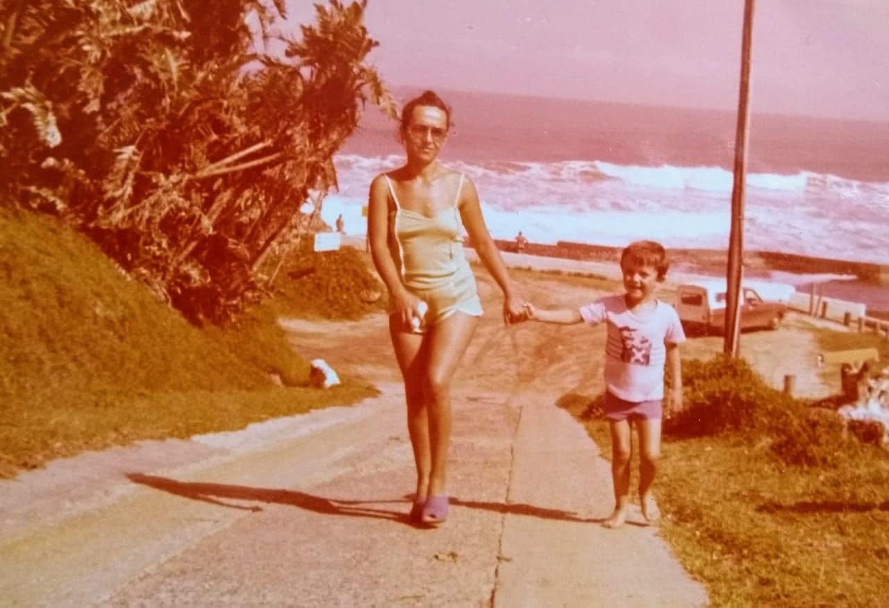 A woman in her thirties holding the hand of a 5 year old boy, walking up a hill, with the sea in the background.
