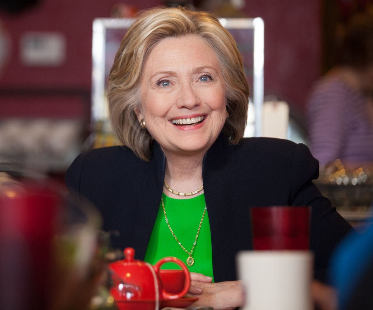 Hillary Clinton seated at a table smiling in 2015. 