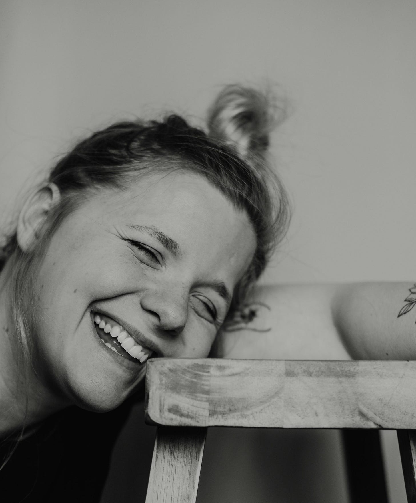 grayscale photo of woman smiling and leaning towards stool