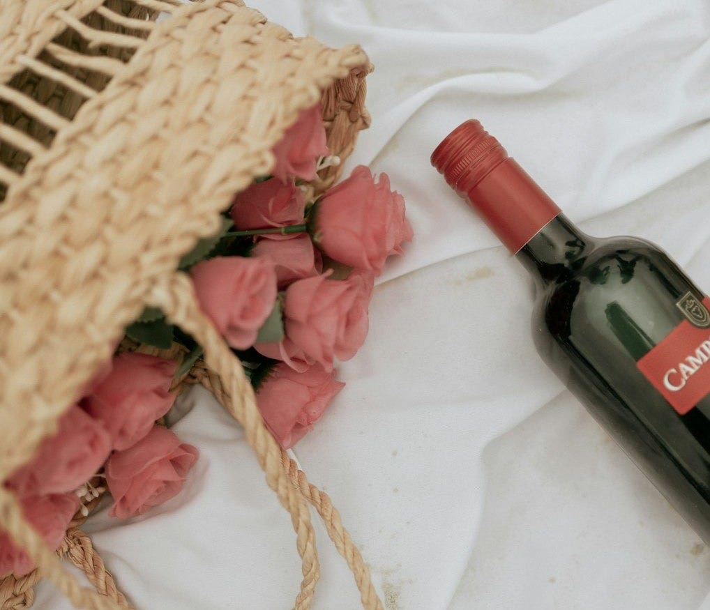 A bottle of wine and a straw bag on a bed