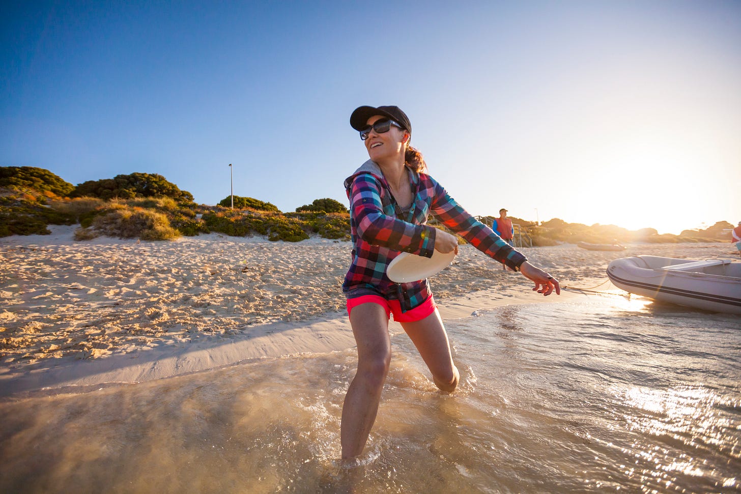 Woman standing on a beach at the edge of the water getting ready to throw a frisbee.