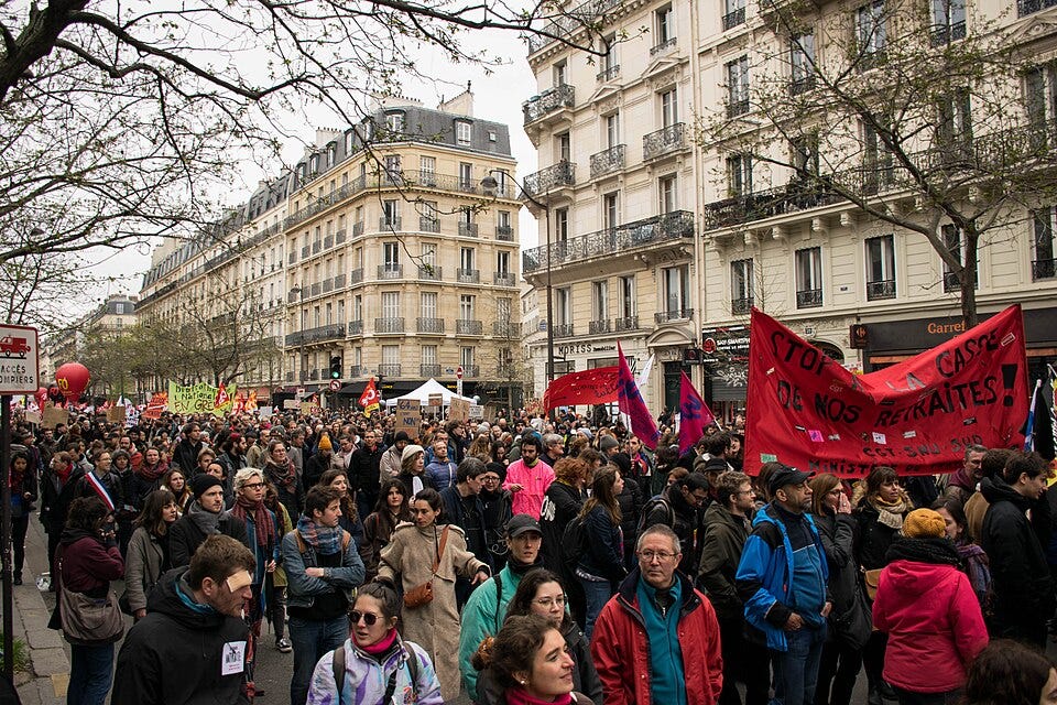 French pension protests Tens of thousands of protesters filling a Paris boulevard on March 28, 2023, demonstrating against pension reform — banners, flags, and crowds stretching beyond the frame, representing a political culture in which collective action remains a civic reflex rather than a career liability.