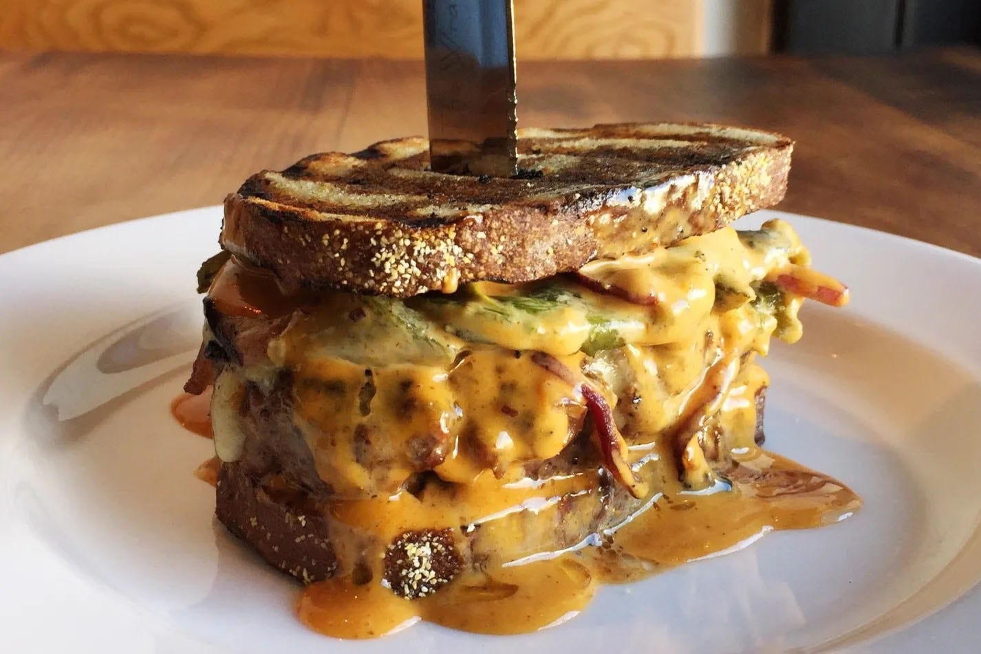 Burger dripping in cheese and sauce in between two pieces of toast.