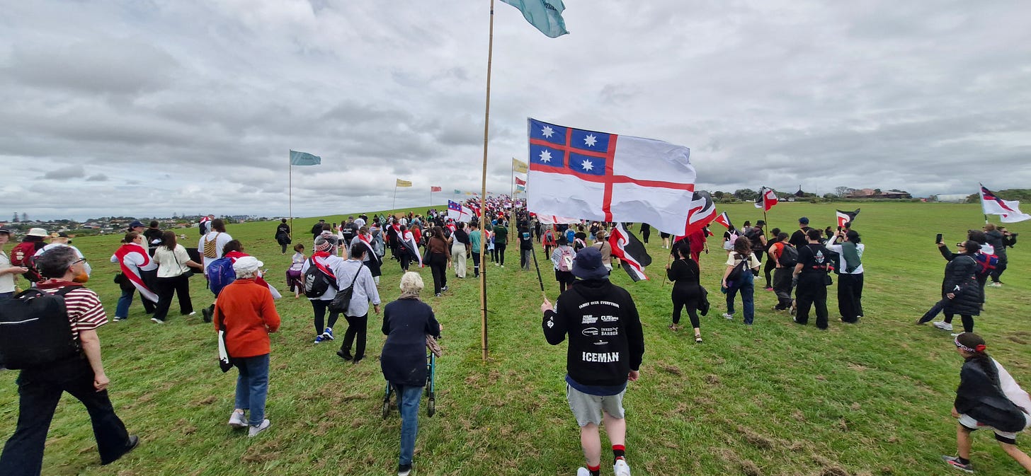 people streaming towards Ōrākei Marae on the hill heading towards the entrance. there are multiple flags