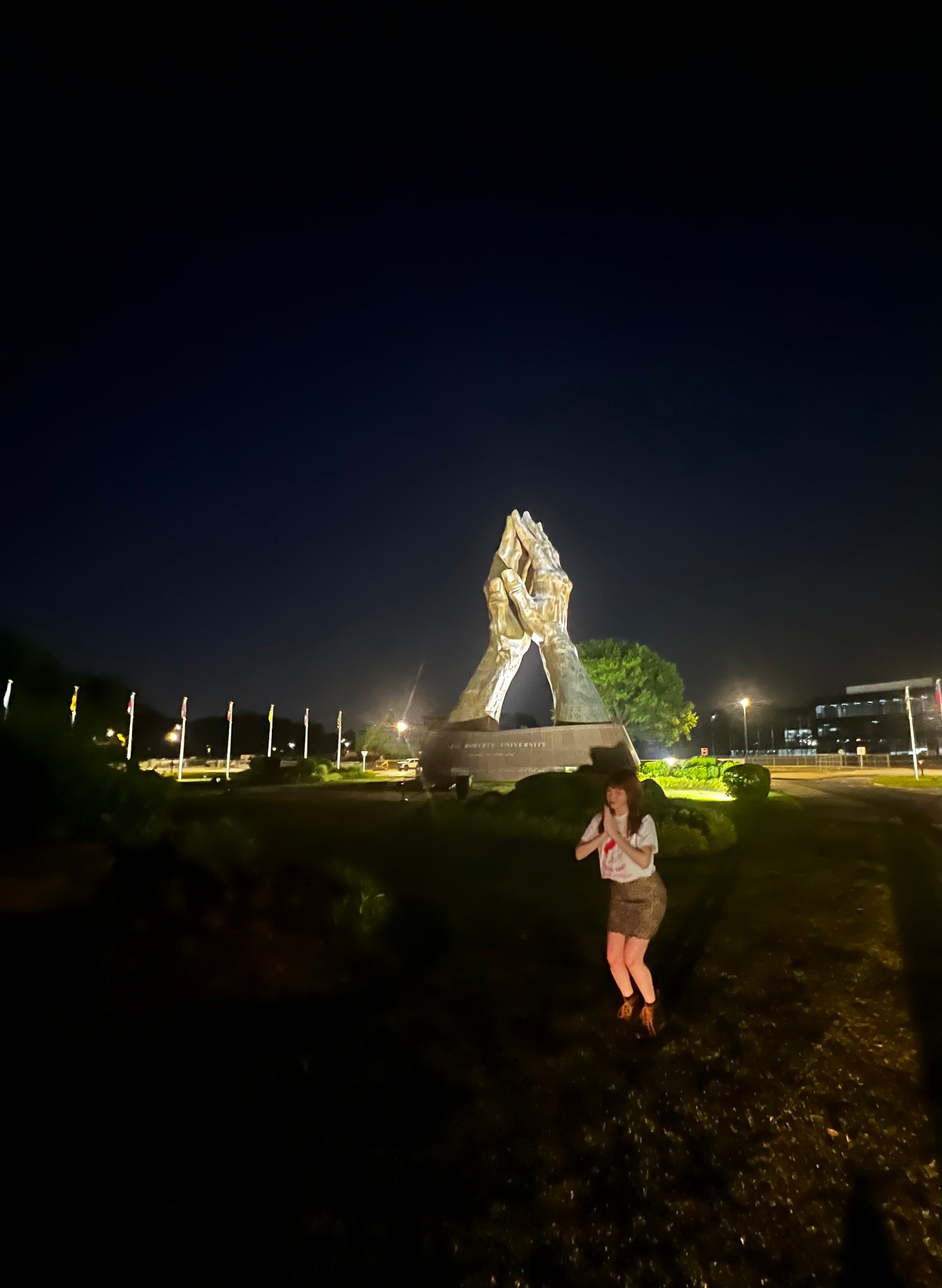 Alice gives prayer hands in front of a giant figure of prayer hands.
