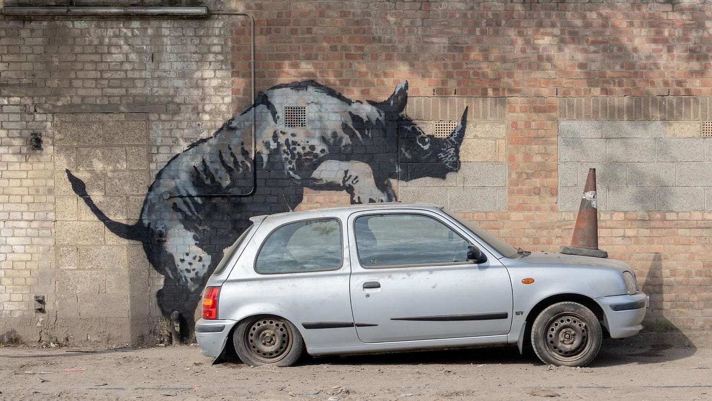 Artwork depicting a rhinoceros climbing on top of a real Nssan Micra car  