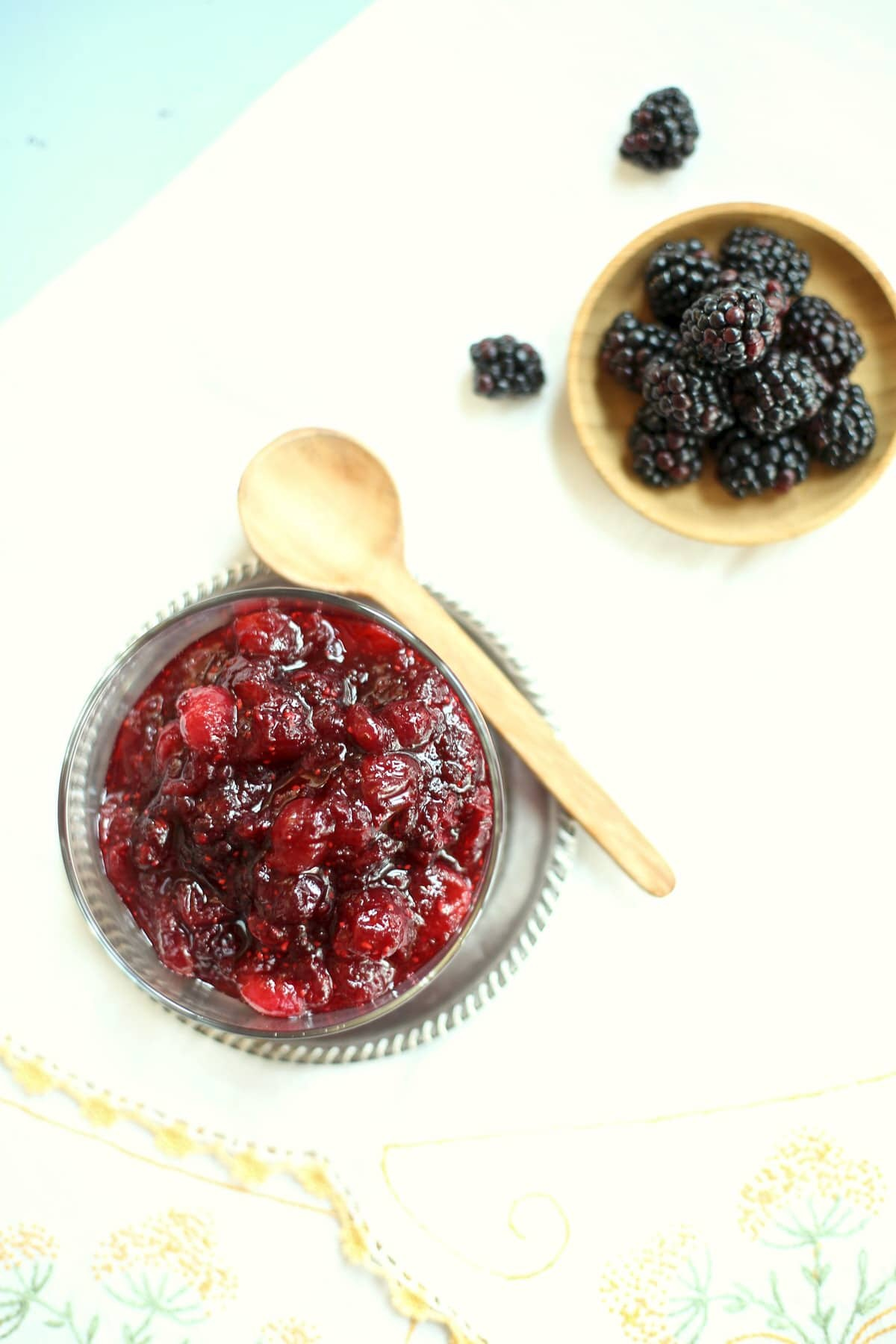 cranberry sauce in a silver and black dish, and fresh blackberries in a small wooden bowl on a table.  cranberry sauce in a silver and black dish, and fresh blackberries in a small wooden bowl on a table.
