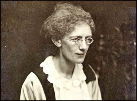 A black and white photo of an elderly woman with her hair pulled back in a bun, wearing wire-rimmed glasses