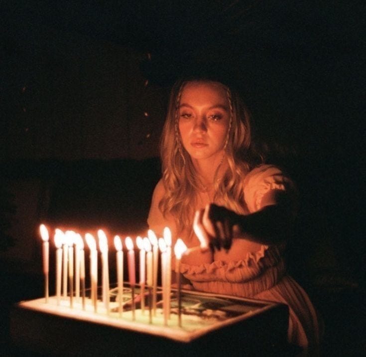 This may contain: a woman sitting in front of a cake with lit candles