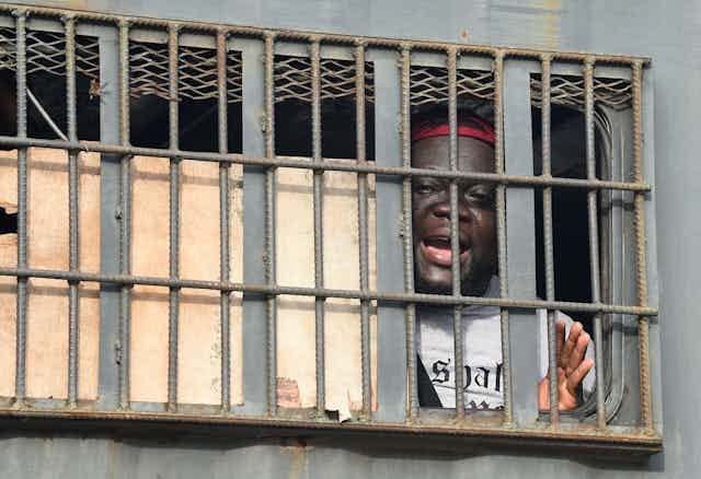 An African man speaks from behind bars in a police van. An African man speaks from behind bars in a police van.