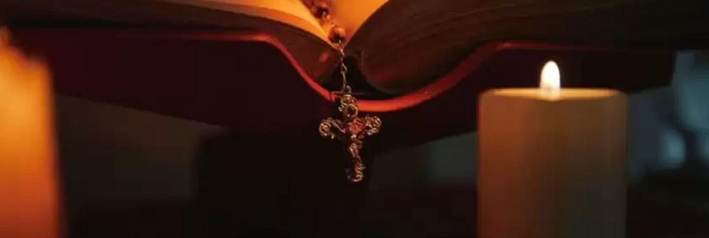 cross hanging from rosary running down the spine of a book with a candle in front cross hanging from rosary running down the spine of a book with a candle in front