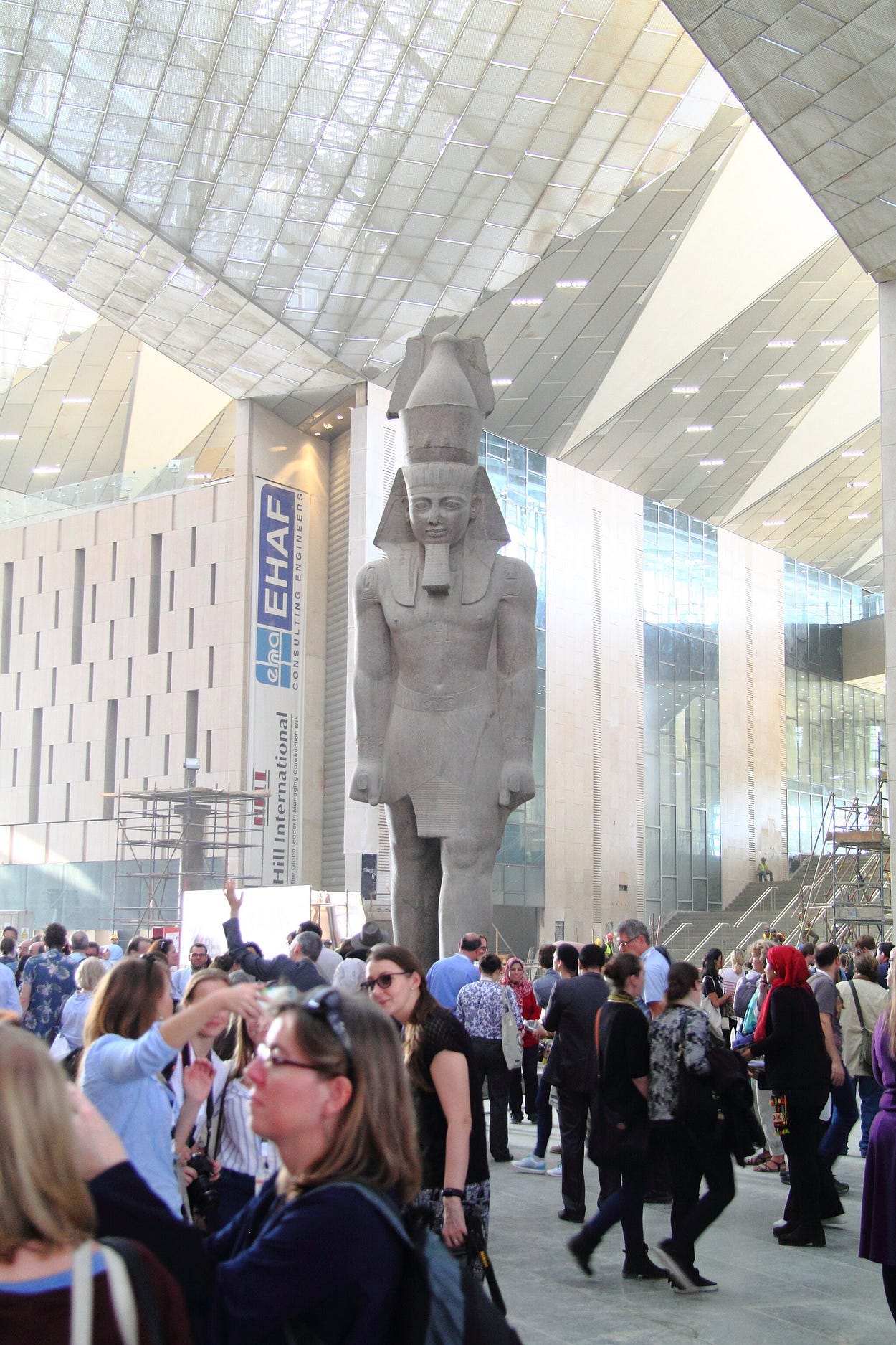 Huge glass and steel entry hall with tremendous ancient statue towering over crowd of visitors. Huge glass and steel entry hall with tremendous ancient statue towering over crowd of visitors.
