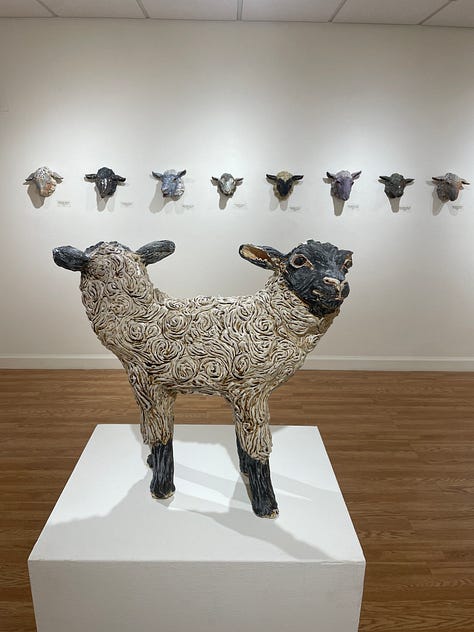 Installation views of a gallery with several artworks depicting sheep. All works are made of ceramic with fiber attachments connecting them together.
