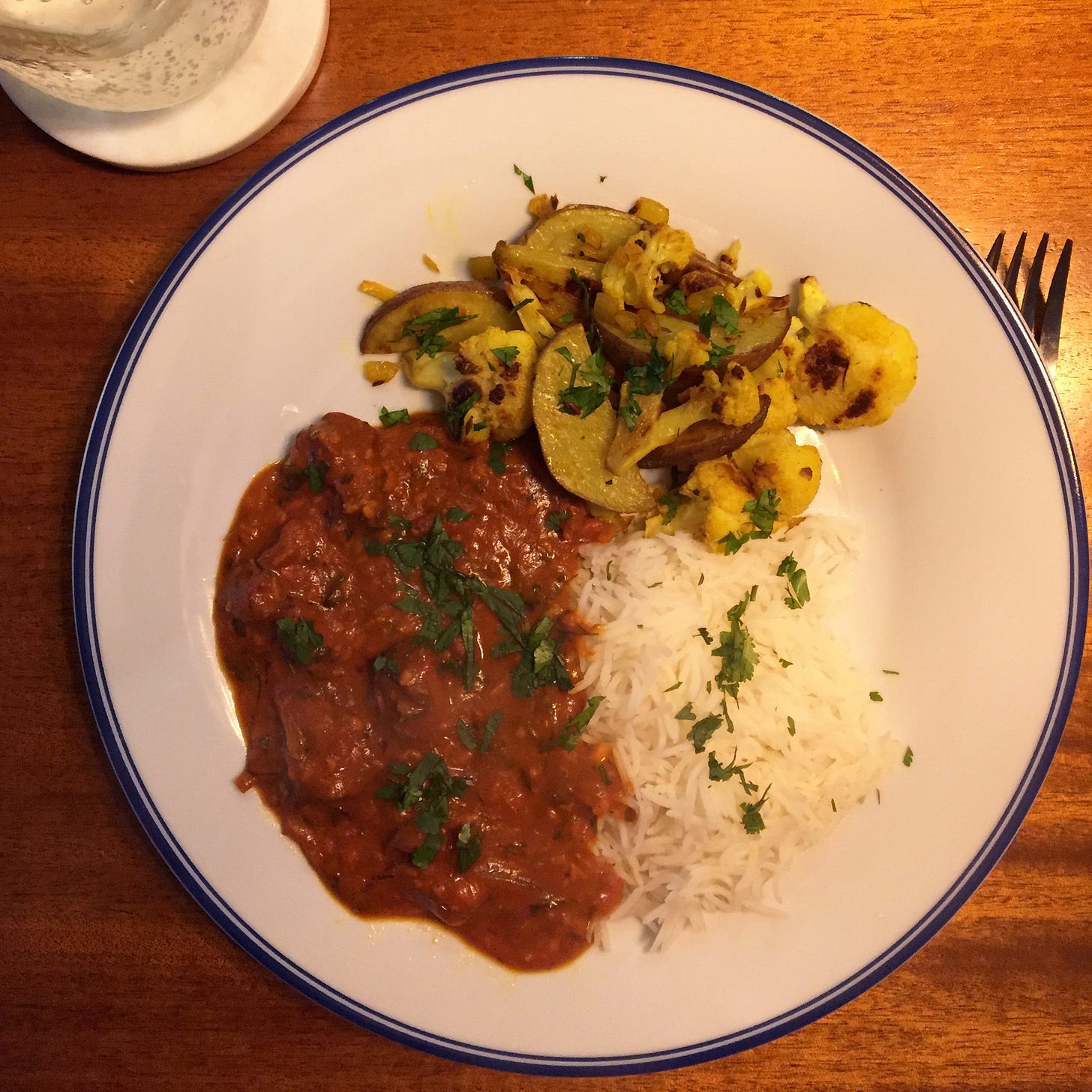 A plate with piles of basmati rice, aloo gobi, and butter chicken in a thick sauce. Cilantro is sprinkled across the top.