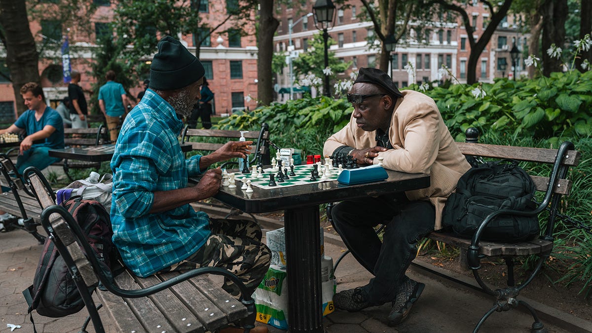 Two men playing chess at a table in a downtown urban park area Two men playing chess at a table in a downtown urban park area