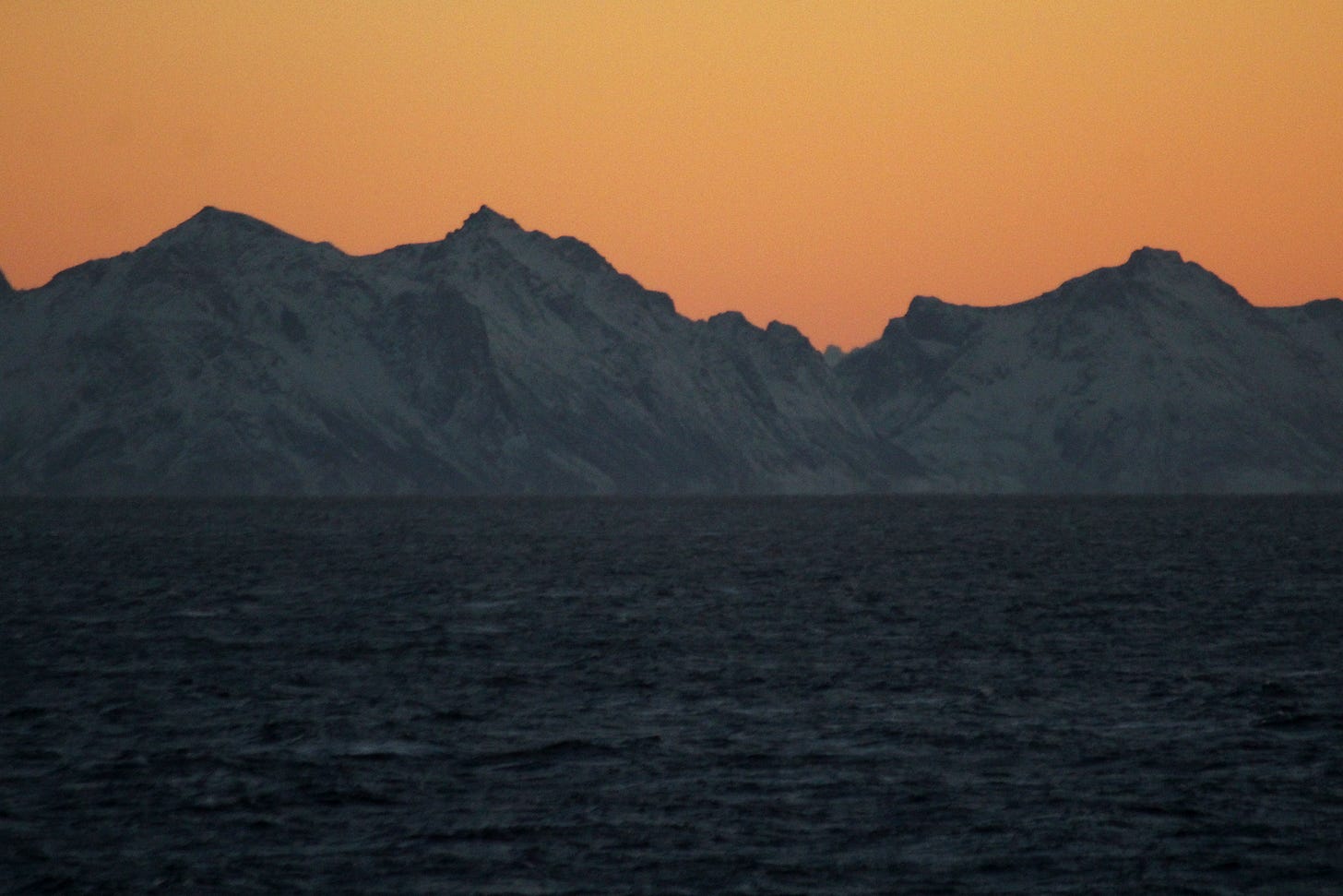 An image of a frozen Norwegian landscape at sunset above a dark sea