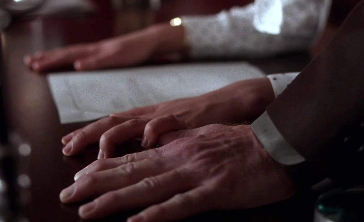 Three white hands palm-down on a desk. Still from Secretary (2002) Three white hands palm-down on a desk. Still from Secretary (2002)