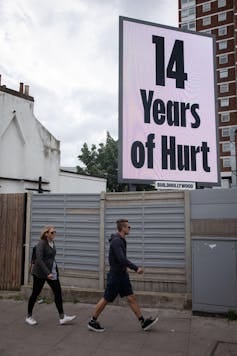A poster reading '14 years of hurt' with two people walking past. A poster reading '14 years of hurt' with two people walking past.