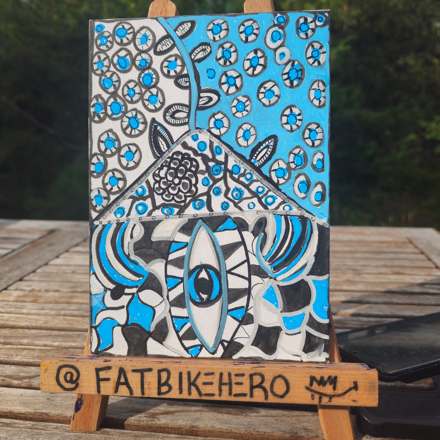 Front (recto) alt text: “Blue, black, and white hand-painted canvas by FatbikeHero titled The Eyed House, featuring a central elongated eye beneath a triangular house shape, surrounded by many small eye-like circles, painted in a graphic, imperfect human-made style.” Front (recto) alt text: “Blue, black, and white hand-painted canvas by FatbikeHero titled The Eyed House, featuring a central elongated eye beneath a triangular house shape, surrounded by many small eye-like circles, painted in a graphic, imperfect human-made style.”