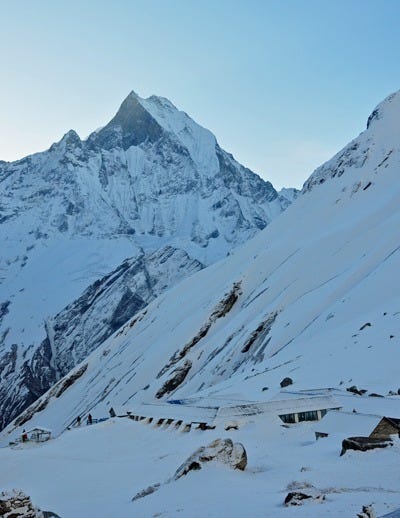 Annapurna Base Camp covered in snow during the cool dawn light. The huge mountains tower in the background.