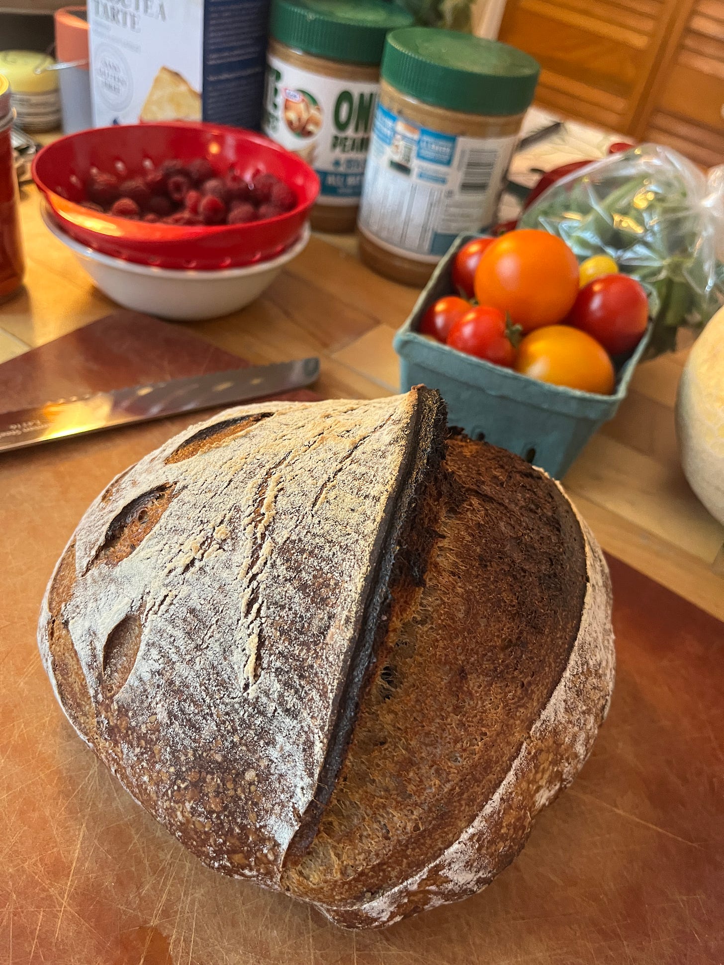 A pretty loaf of sourdough bread on my counter with fresh tomatoes and berries from the market in baskets nearby
