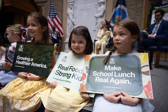 Three girls hold Growing a Healthier America, Real Food Strong Kids, and Make School Lunch Real Again signs