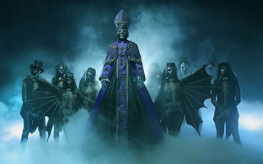 Figures in dark, skeleton costumes and bat-like wings stand in fog. Central figure in purple, ornate robe and mitre. Eerie, mysterious mood.