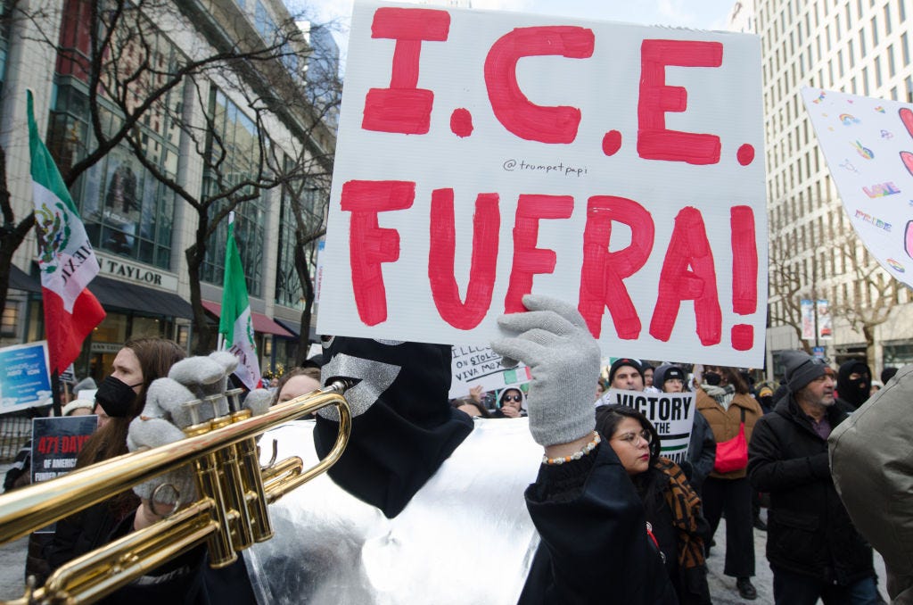 a protestor wearing a black mask and blowing into a trumpet holds a sign reading "ICE FUERA" a protestor wearing a black mask and blowing into a trumpet holds a sign reading "ICE FUERA"