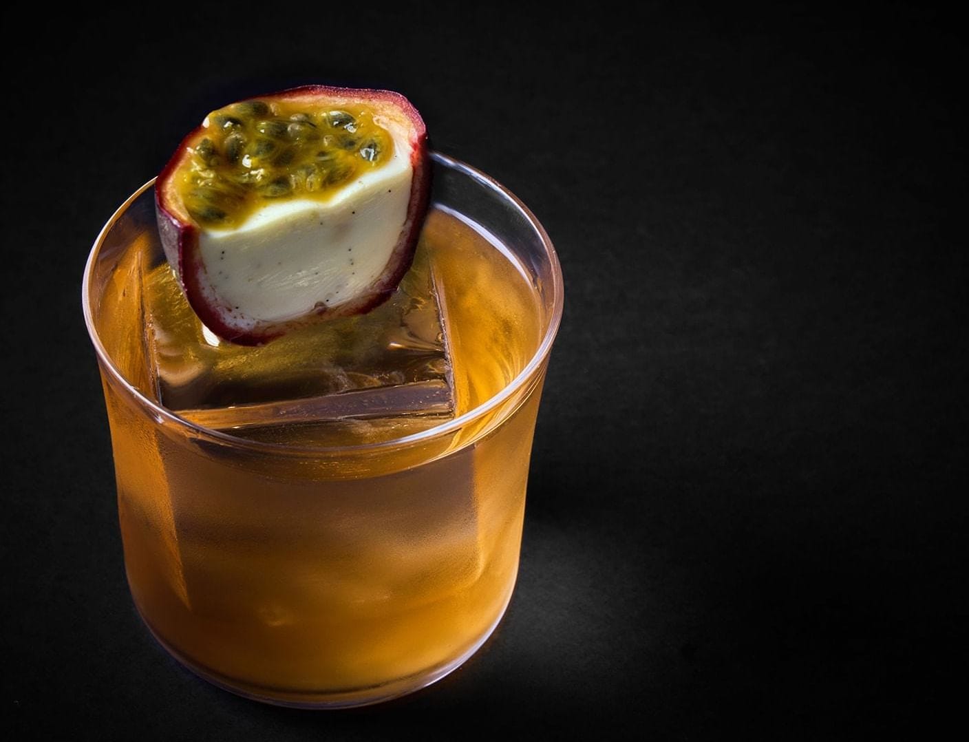 A sophisticated cocktail with a large ice cube, garnished with a fresh passion fruit half at The Londoner Hotel A sophisticated cocktail with a large ice cube, garnished with a fresh passion fruit half at The Londoner Hotel