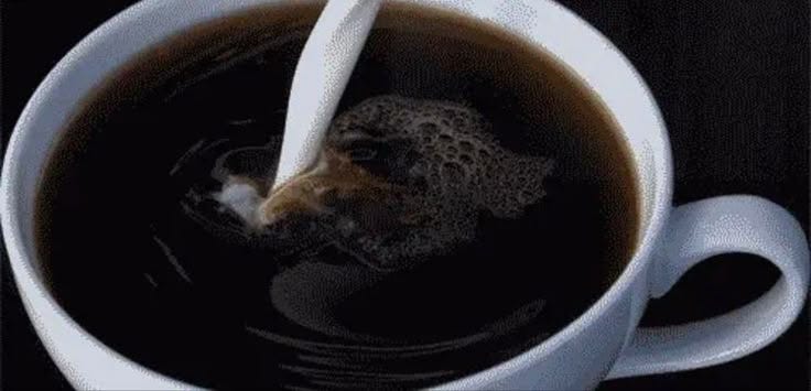 This may contain: a white cup filled with black liquid and a spoon sticking out of it's side
