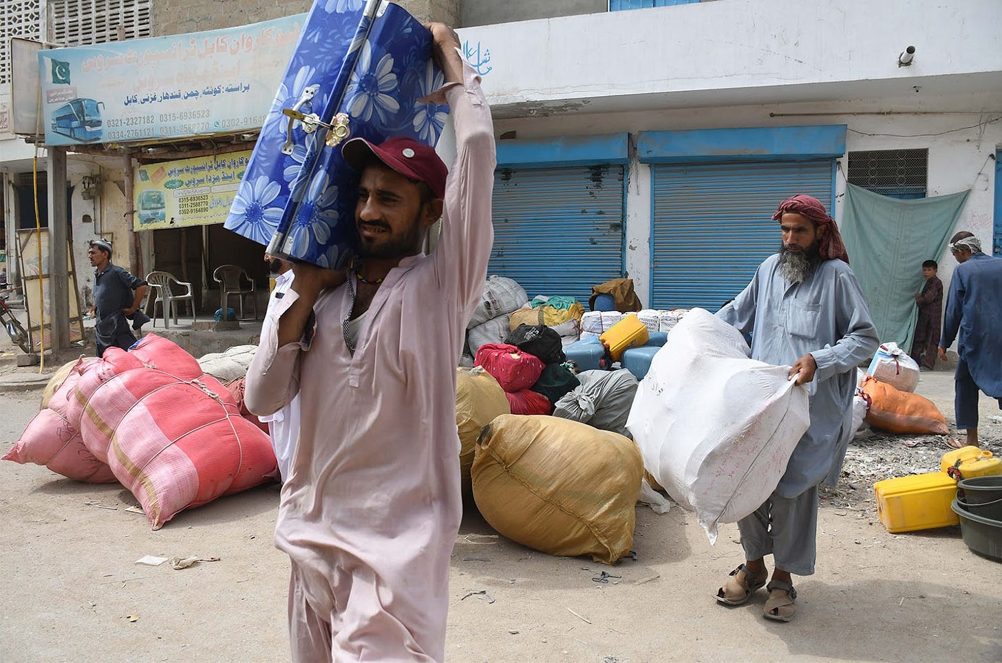 Pictured are two Afghan refugees carrying packaged, one carries a blue luggage over his shoulder and another a white sack. They are outside of a building to leave the Pakistani port city of Karachi and return to Afghanistan following the Pakistani government's decision to deport those illegally staying in the country, in Karachi, Pakistan on October 06, 2023.