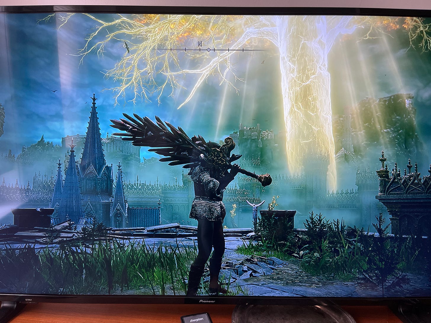 Warrior holding a large sword made of other swords while standing in front of a church and a glowing tree.