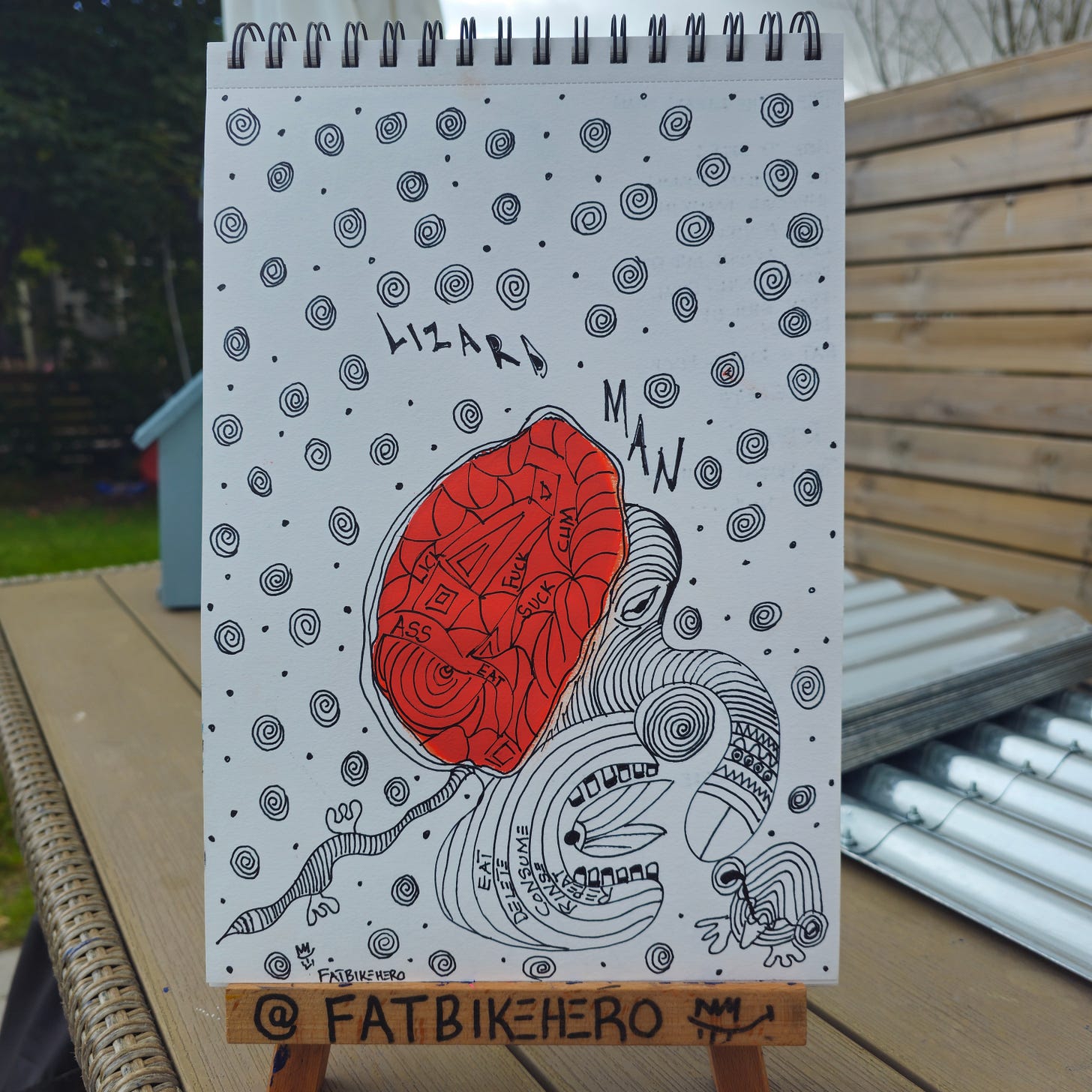 Alt Text: A black and white ink drawing by FatbikeHero titled "Lizard Man" featuring a central red oval filled with words like "LICK," "FUCK," and "SUCK." The surrounding space is filled with spirals and a creature with an open mouth containing the words "EAT," "DELETE," and "CONSUME."