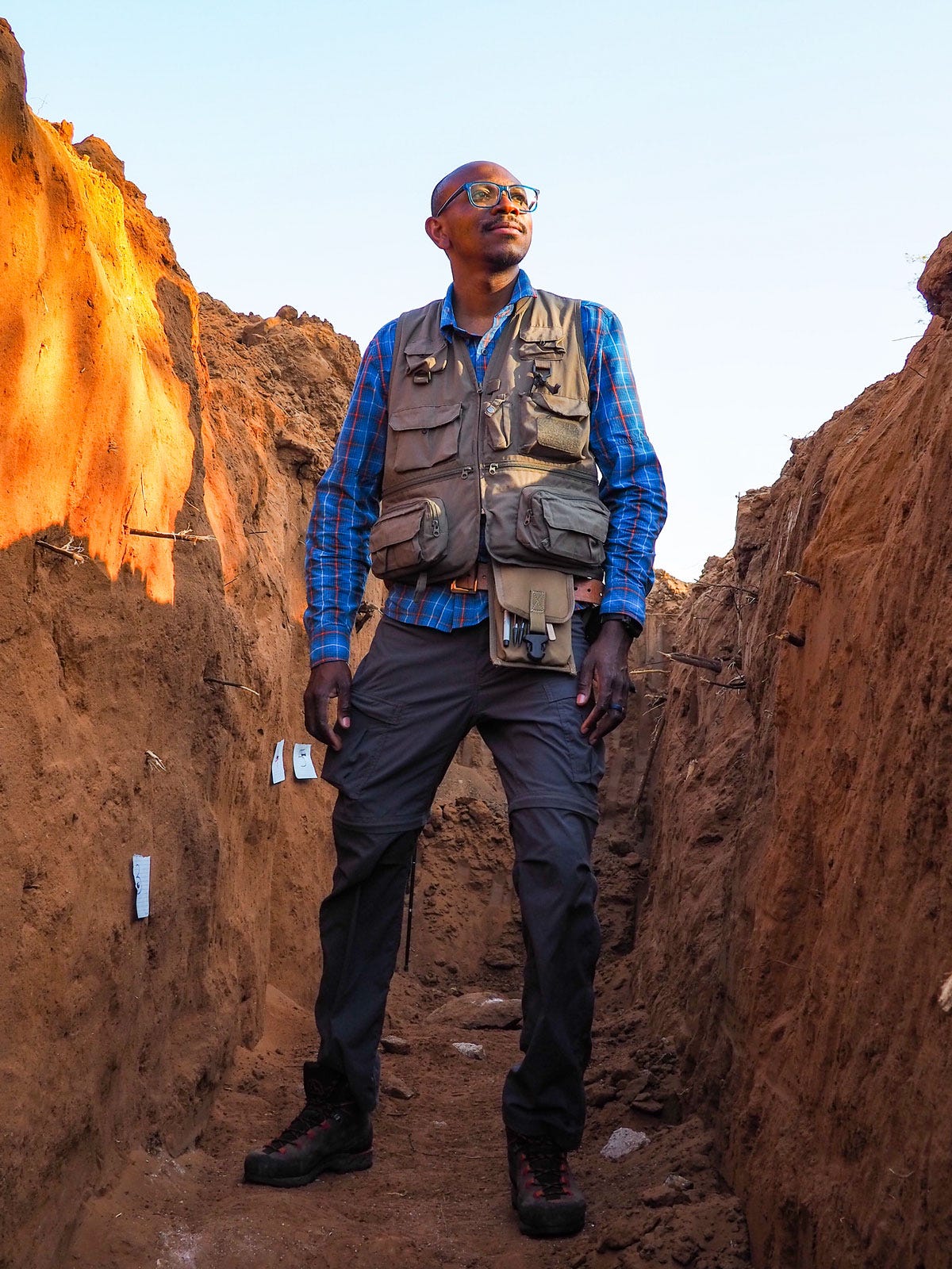 Folarin Kolawole stands in a trench. He is looking slightly up and into the distance.