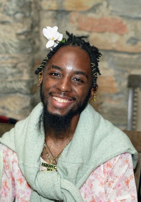 A cute image of me wearing a flower blouse with a mint green cardigan tied prep-like around my shoulders. I'm wearing a gold chain to match the gold jewelry around my ears and hair. I'm also cheesin.