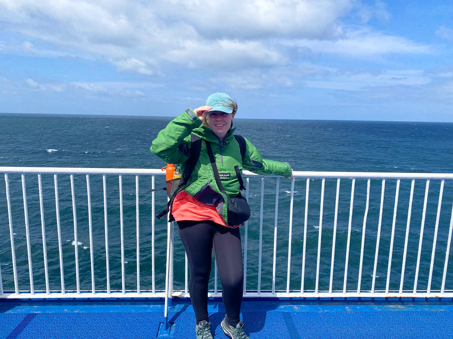Woman in a green jacket and turquoise cap smiling on a ferry deck, leaning against white railings with the open sea behind her. Woman in a green jacket and turquoise cap smiling on a ferry deck, leaning against white railings with the open sea behind her.