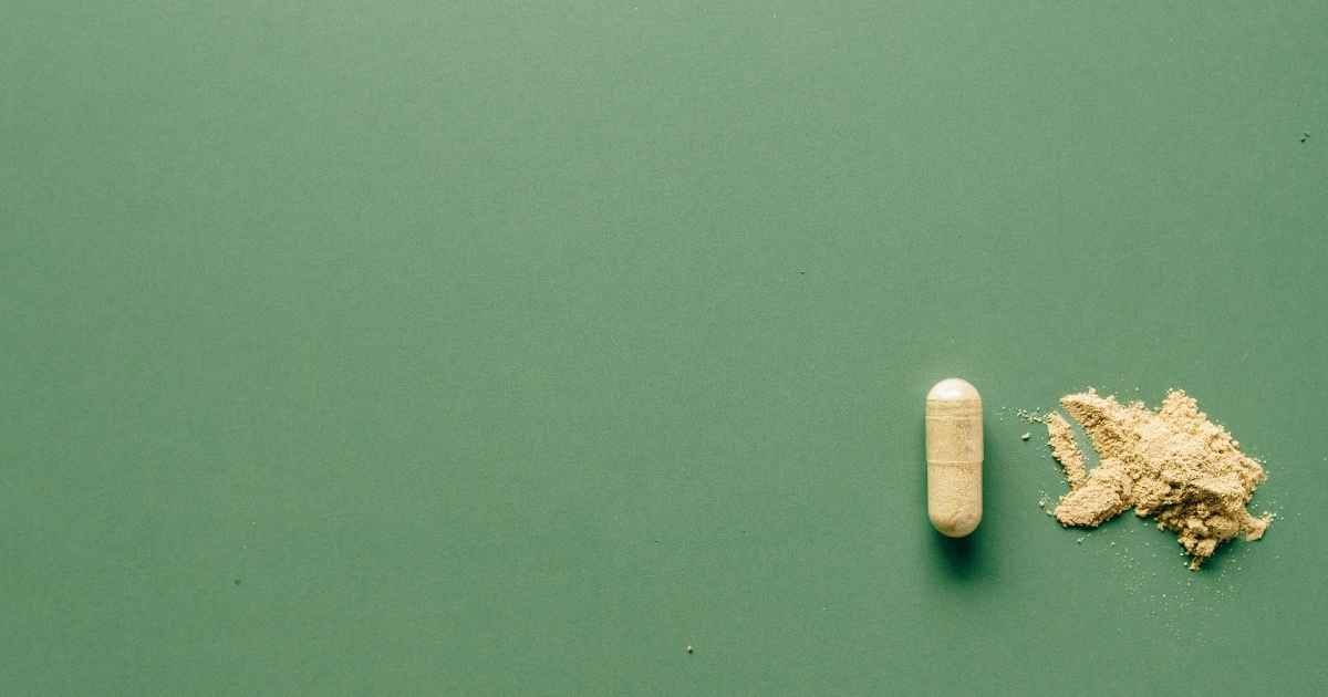 Close-up of herbal supplement capsule and powder on a minimalist green surface