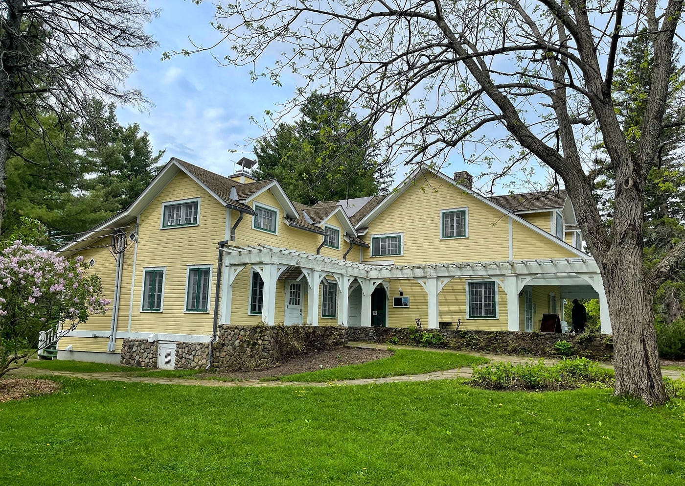 A large yellow-white wooden house with a veranda on a grand green lawn.