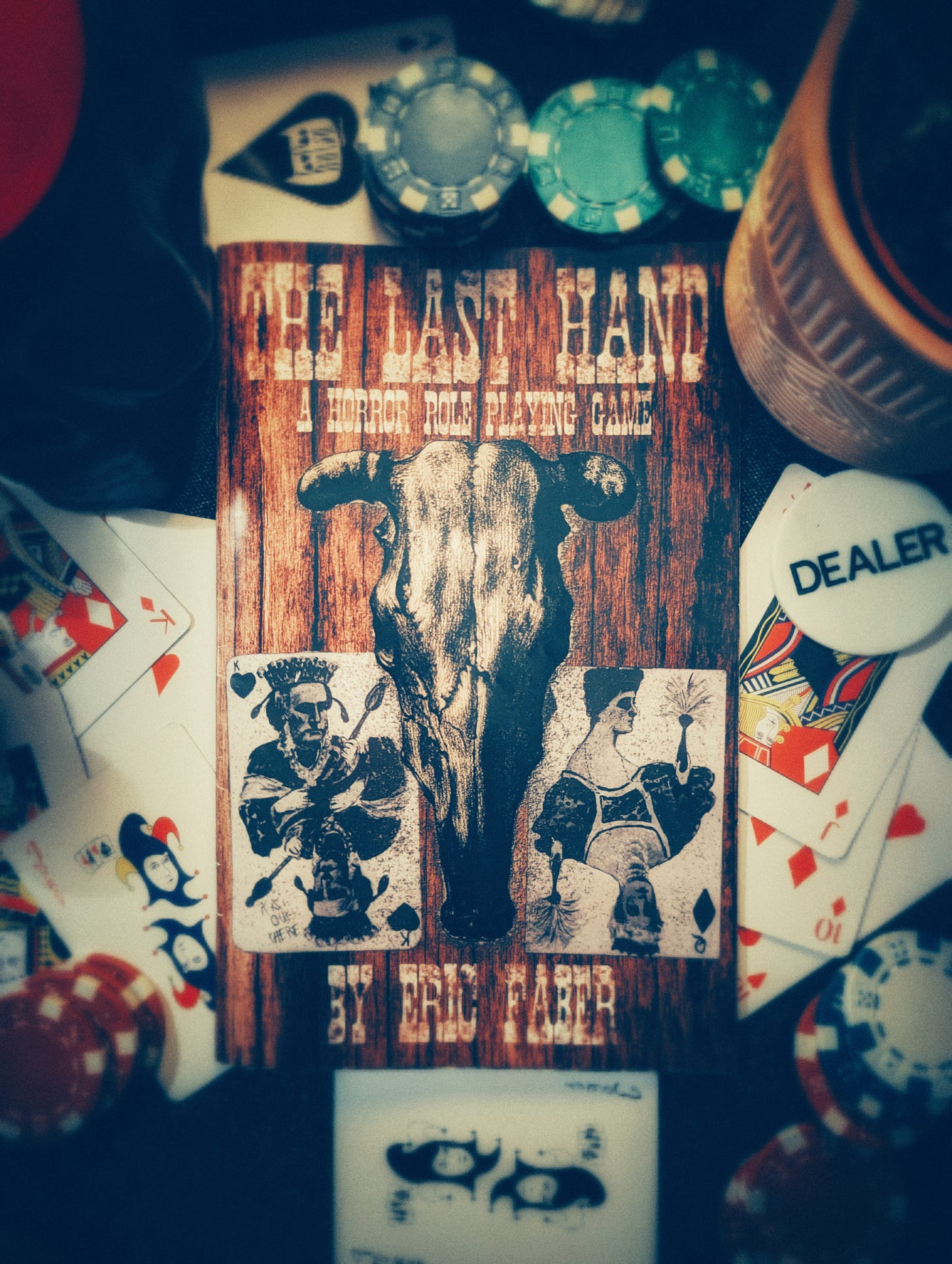 The cover of The Last Hand ttrpg by Eric Faber. Cow Skull on cover flanked by playing cards. The book is surrounded in playing cards and poker chips.