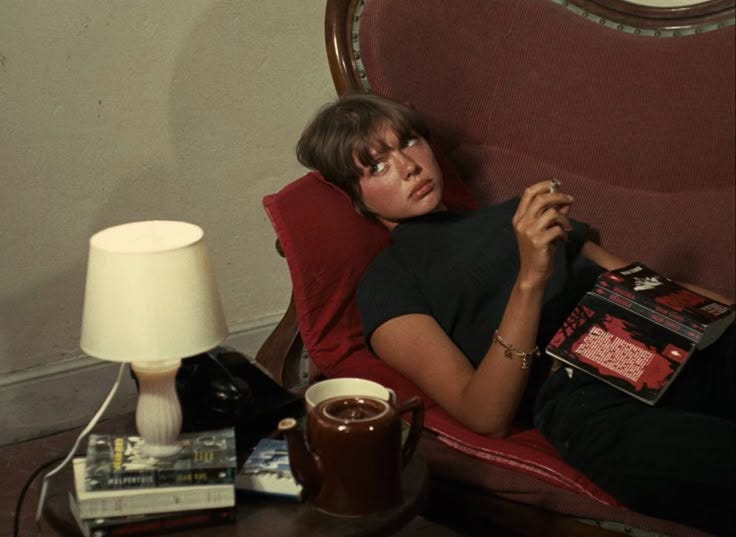 This may contain: a woman laying in a chair with a book and cup on the table next to her