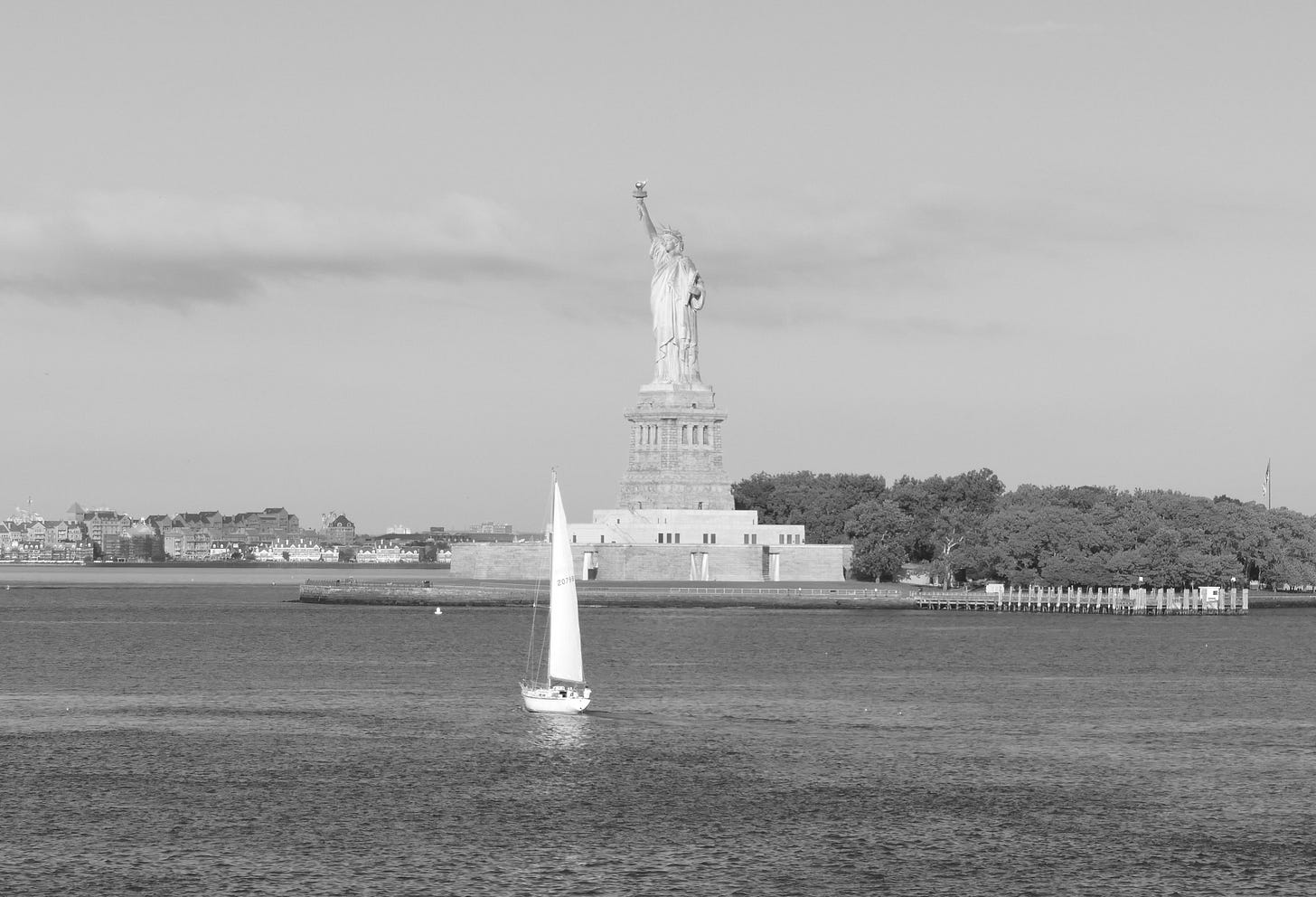 Black and white photo of Statue of Liberty from Staten Island Ferry, with sailboat at sea in foreground