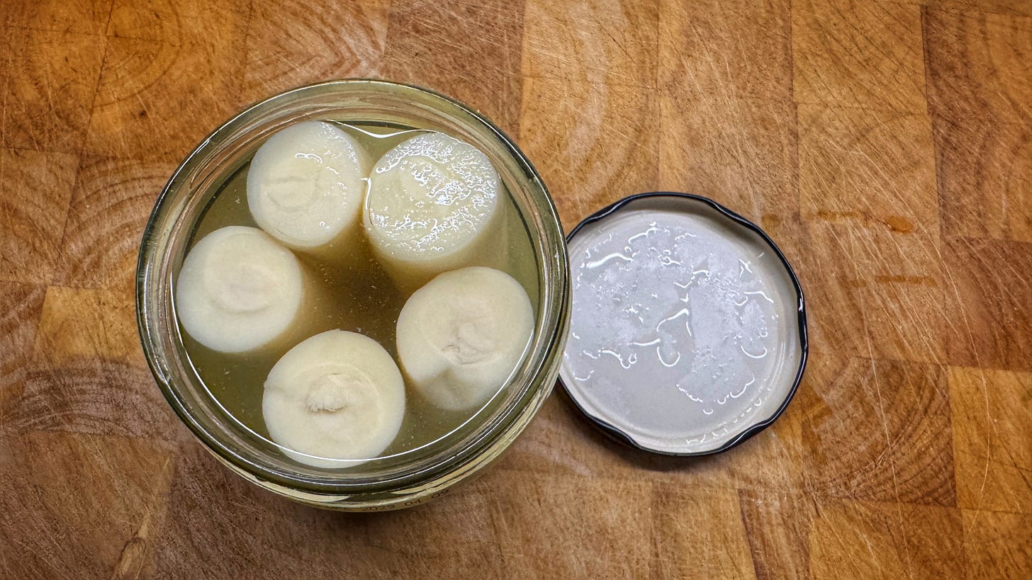 An opened jar of hearts of palm on a wooden cutting board. Seen from above, there are 5 hearts of palm in the jar. The lid of the jar is beside it on the cutting board. An opened jar of hearts of palm on a wooden cutting board. Seen from above, there are 5 hearts of palm in the jar. The lid of the jar is beside it on the cutting board.