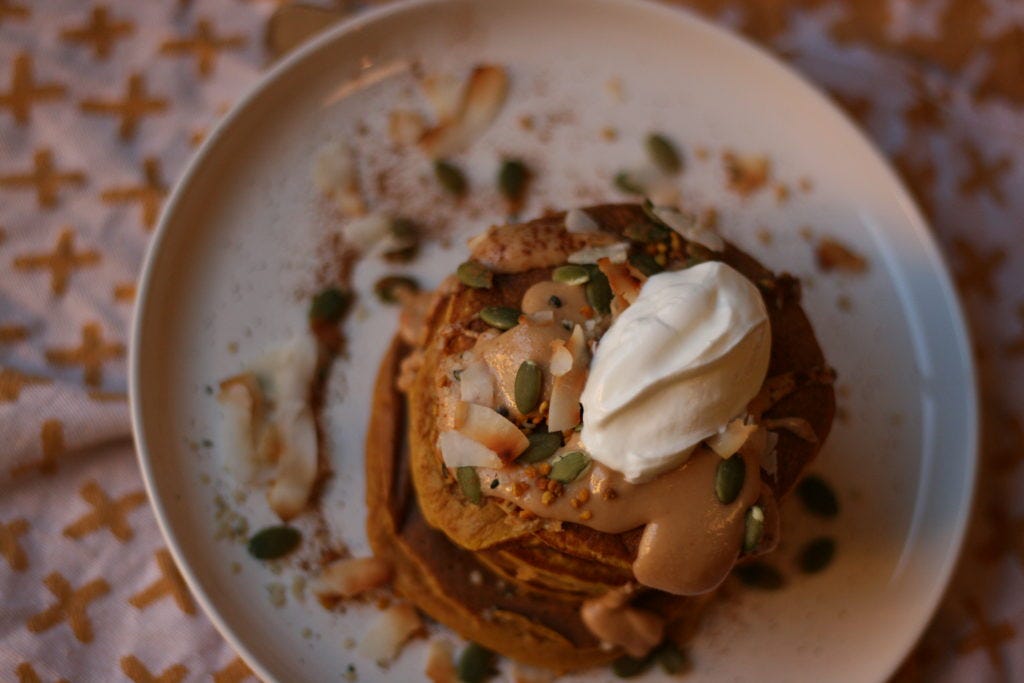 Aerial view of oat pumpkin pancakes, which are topped with pepitas, toasted coconut, almond butter and yogurt.