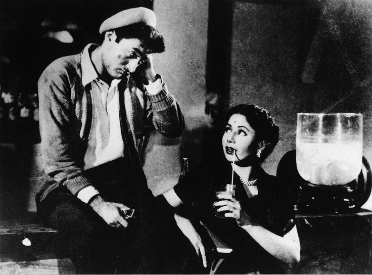 This may contain: a man and woman sitting next to each other in front of a glass filled with liquid