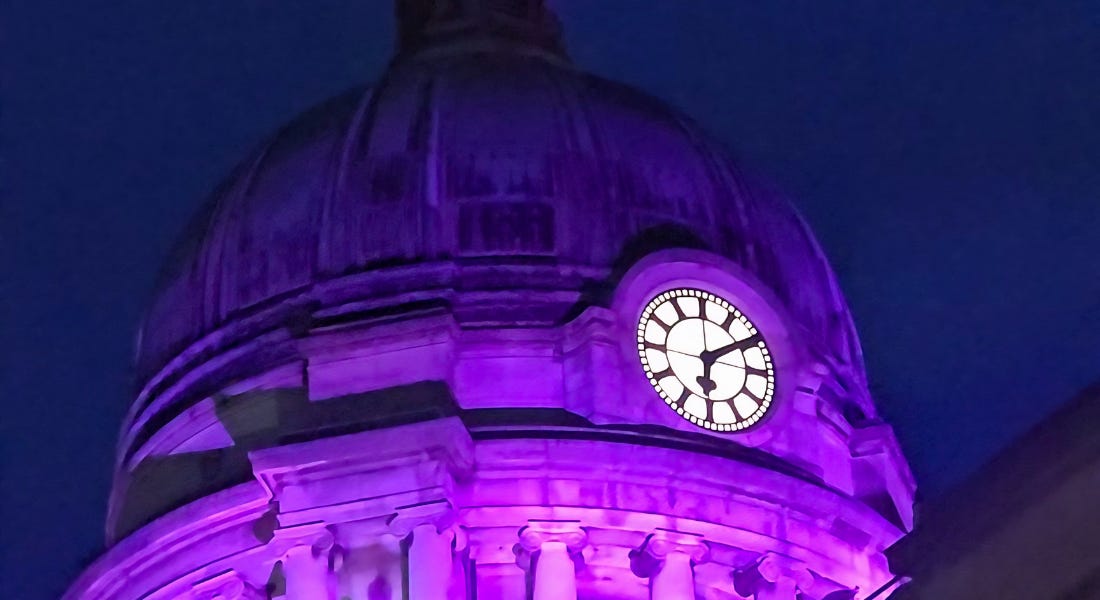 A close-up of a building clock with purple lights lighting it