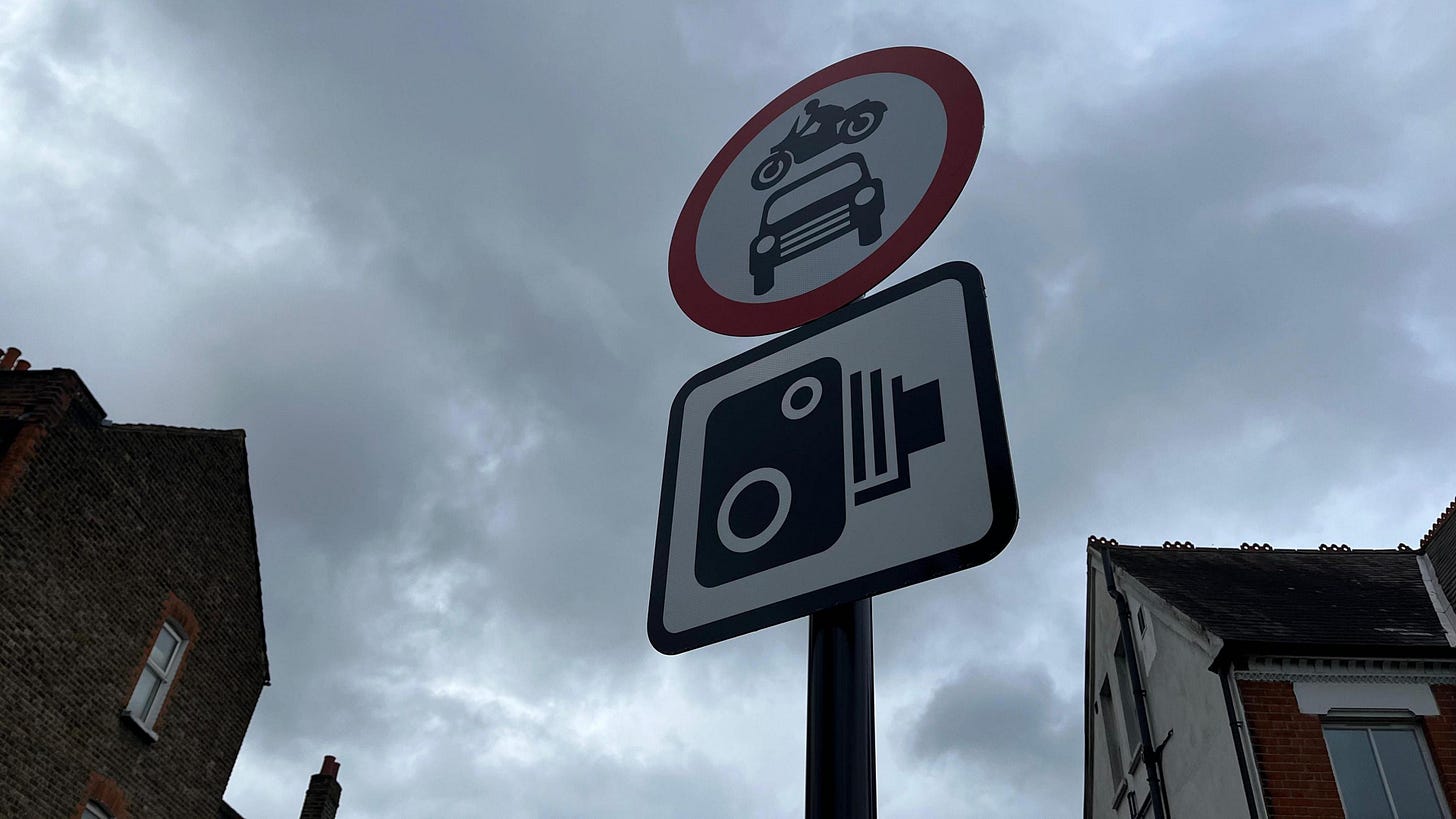 Circular red sign with car and bike inside and square camera sign just below