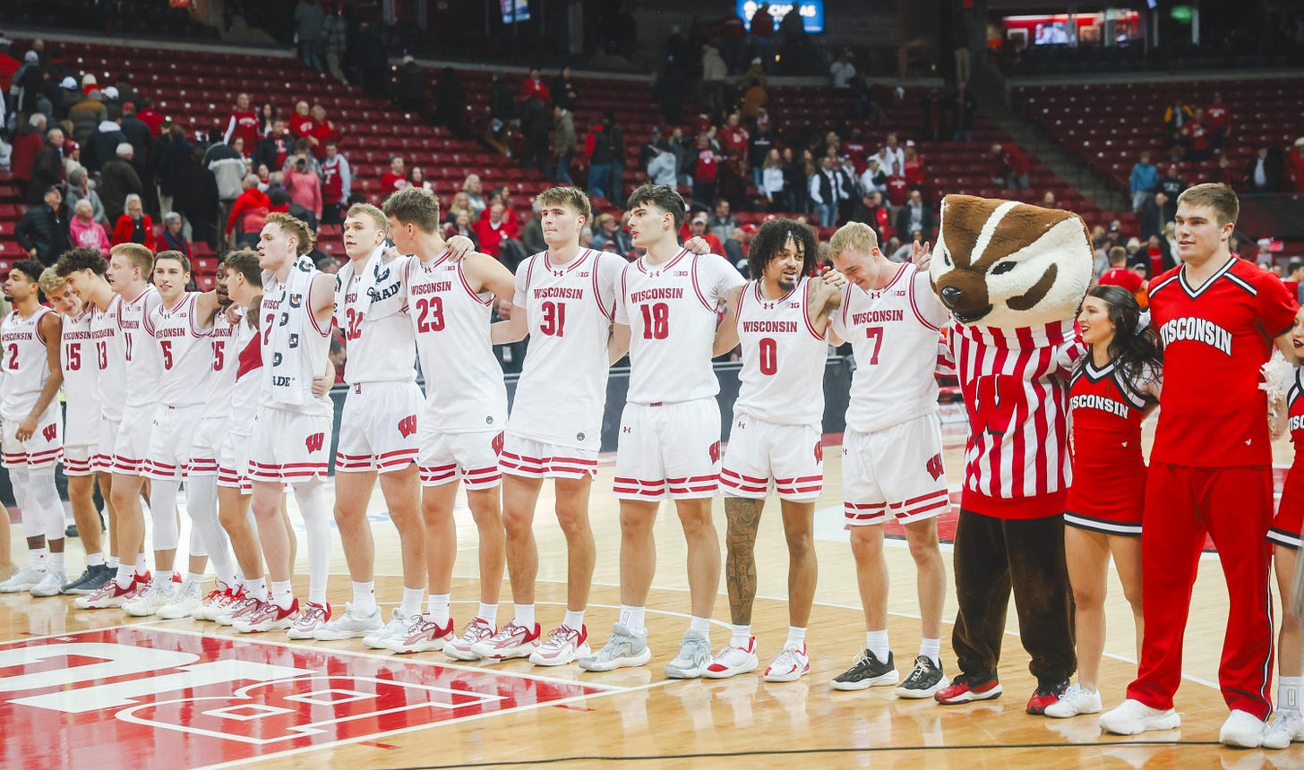 The Wisconsin men's basketball team stands shoulder to shoulder performing the Varsity tradition on the court at the Kohl Center.