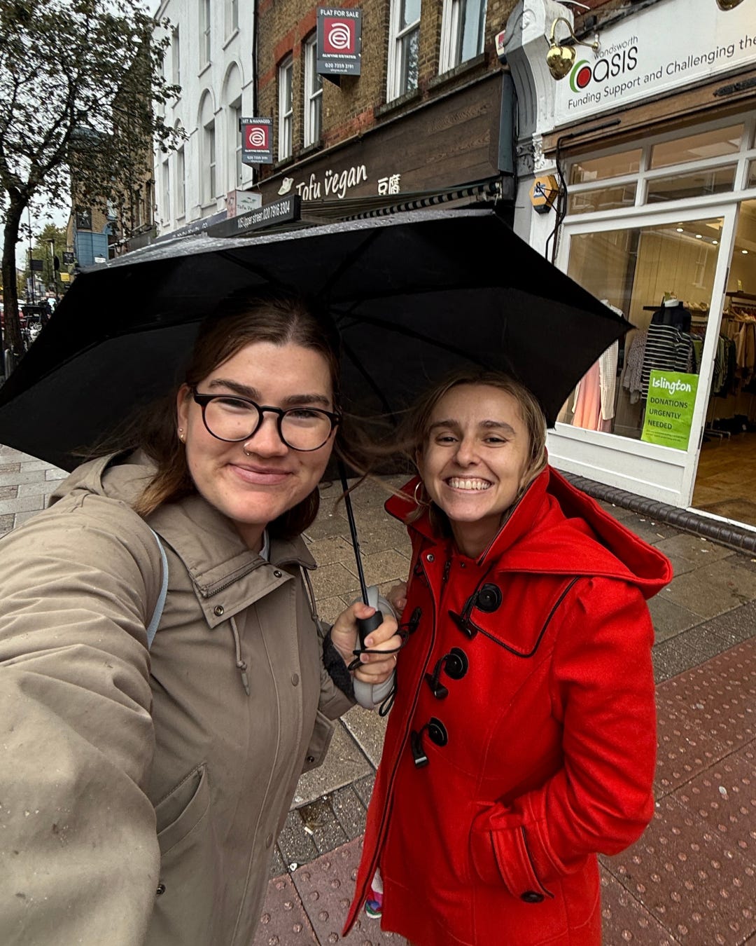 Hannah and Katie standing on a London street under an umbrella