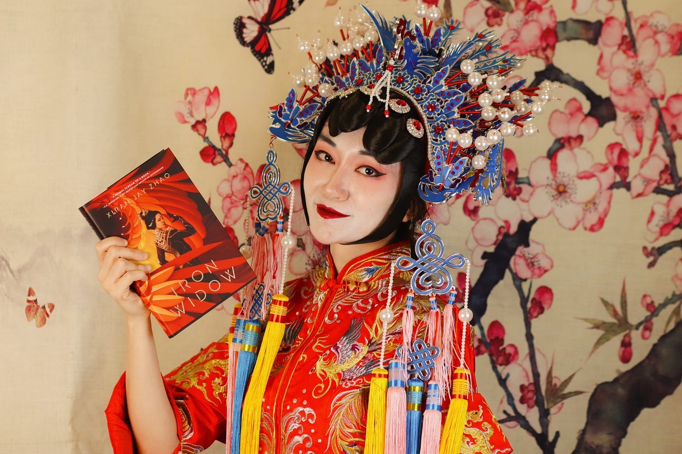 Xiran Jay Zhao dressed fabulously in traditional Chinese garb holding a copy of Iron Widow
